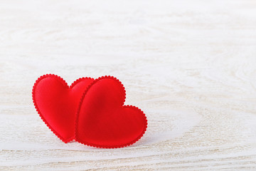 Fototapeta premium Two red silk valentine hearts on a white wooden textured background. Concept love, Valentine's day. Greeting card with copy space.