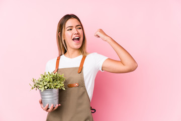 Young caucasian gardener woman in a pink background raising fist after a victory, winner concept.