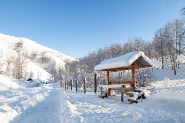 The picturesque landscape with snowdrifts, a hiking trail along the fence with a wooden gazebo in the Altai mountains under a blue sky with snow in winter.