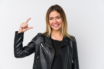 Young caucasian woman wearing a black leather jacket holding something little with forefingers, smiling and confident.