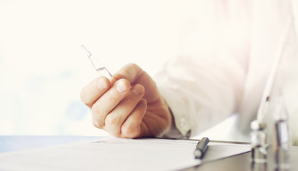 A man signs a medical document. Medical equipment on the table. Stethoscope and ampoules with syringes. Makes notes in the office. Medical center.