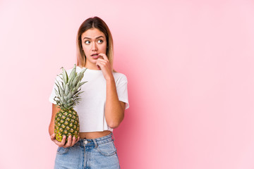 Young caucasian woman holding a pineapple relaxed thinking about something looking at a copy space.