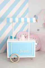Cart with Candy Bar. Children zone with sweets: lollipops, ice cream and candy bar. Children room with blue stripe background. candy stall photo zone.  Decorated room for a birthday. holiday decor