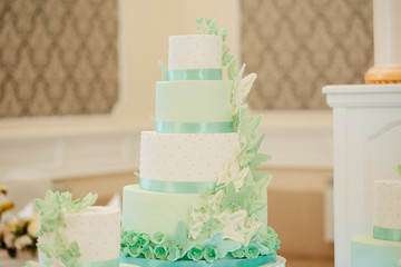 Beautiful wedding cake. The combination of white and turquoise. Decorated with beautiful butterflies. Wedding cake on restaurant interior background. Sweet cake on a festive buffet. 