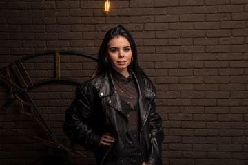 Naklejka premium brunette in a black leather jacket on a background of a brown brick wall and a clock