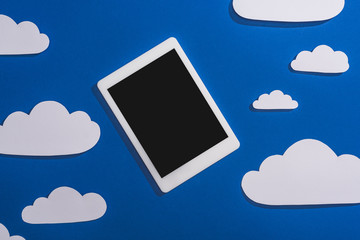 top view of white paper cut clouds and digital tablet on blue background