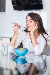 Smiling happy woman having a relaxing healthy breakfast at home sitting at kitchen table