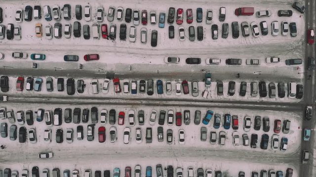 Aerial top view of large car park with many autos near modern mall or shopping center in snowy weather in winter. Parking lots with rows of vehicles, drone footage