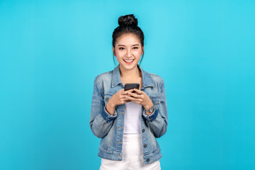 Portrait of Happy asian woman feeling happiness and looking camera holding smartphone on blue background. Cute asia girl smiling wearing casual jeans shirt and connect internet shopping online