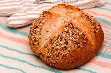 Freshly baked whole grain loaf of bread sprinkled with seeds of flax, sesame, sunflower seeds on linen towel. Healthy home baking concept. Close-up