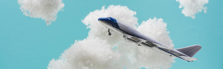 toy plane flying among white fluffy clouds made of cotton wool isolated on blue, panoramic shot