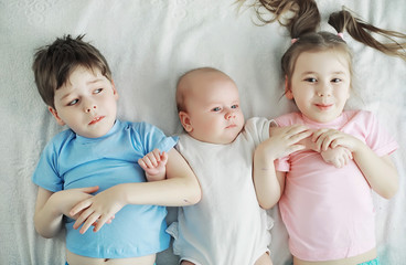 Children lie on the bed next to the newborn baby, little sister.
