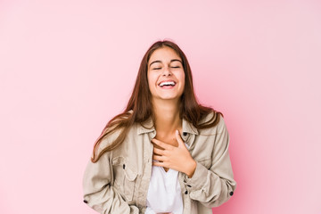 Young caucasian woman posing in a pink background laughs happily and has fun keeping hands on stomach.