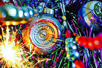 Fototapeta na wymiar Vintage silver Christmas ball on colorful Christmas tinsel between threads of retro glass beads with yellow sparks fireworks. Bright beautiful colorful new year wallpaper. Selective focus