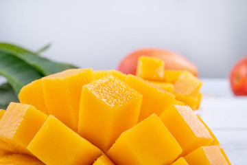 Fresh mango,beautiful chopped fruit with green leaves on bright wooden table background. Tropical fruit design concept, close up, copy space.