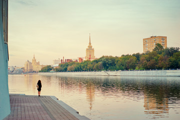 Moscow promenade. Lone girl stands at the edge of an embankment at Moskva river.