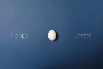 White easter egg with happy easter word, holiday concept. Blue background. Top view