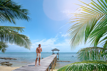 Enjoying suntan and vacation. Young strong man standing on the wooden beach pier.