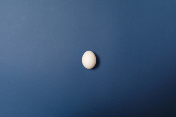 Single white egg on blue background. Holiday concept. Happy Easter
