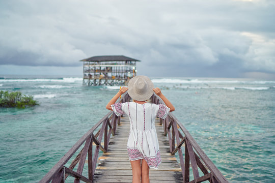 Vacation on tropical island.  Back view of young woman in hat enjoying sea view from wooden bridge terrace, Siargao Philippines