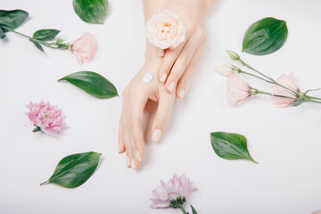 Concept spa skin care. Top view cosmetic cream on female hands with pink flowers on white background, flat lay