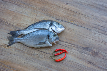 Raw dorado or sea bream fish on wooden table with red hot chili peppers, top view. Space for text