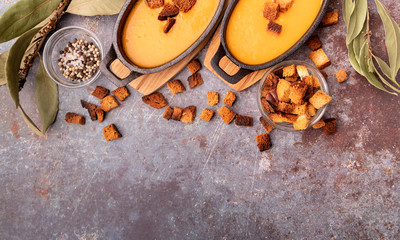 Pumpkin soup with croutons in iron pots decorated with croutons, laurel leaves and spices top view on dark background with copy space