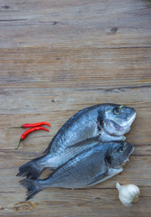 Raw dorado or sea bream fish on wooden table with vegetables, top view. Space for text