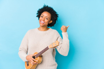 Young african american woman playing ukelele isolated points with thumb finger away, laughing and carefree.