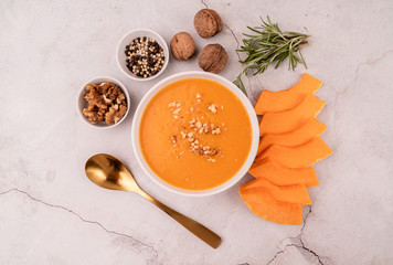 Pumpkin soup with walnuts in white bowl decorated with pumpkin slices and spices top view on white marble background