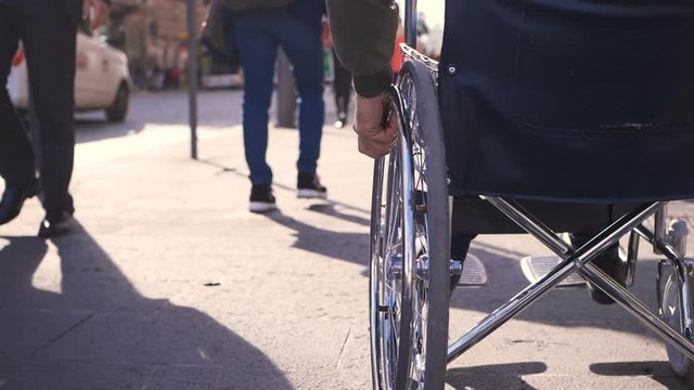 young paraplegic's arms pushing his wheelchair on sidewalk