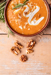 Fototapeta premium Pumpkin soup with creme in brown bowl decorated with walnuts top view with copy space on wooden background