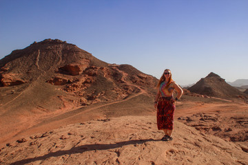 Fototapeta na wymiar Caucasian woman hippie red-haired traveler with glasses posing against the backdrop of the desert in Timna National Park, Israel,