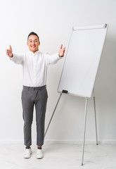 Young latin coaching man with a whiteboard isolated feels confident giving a hug to the camera.