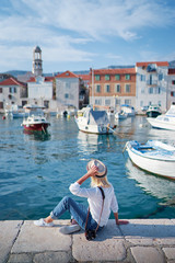 Fototapeta na wymiar Tourism concept. Young traveling woman enjoying the view of Kastel Castle sitting near the sea on Croatian coast.