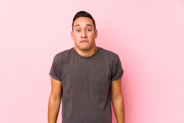 Yooung latin man posing in a pink backgroundshrugs shoulders and open eyes confused.