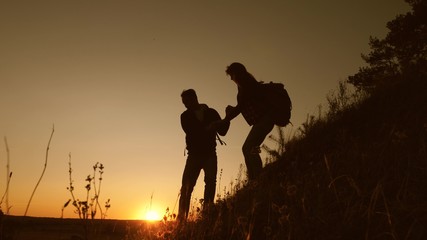 Travelers descend from mountain at sunset, hold hands. adventure and travel concept. teamwork of business people. Hiker man holds out his hand to woman traveler descending from top of hill.