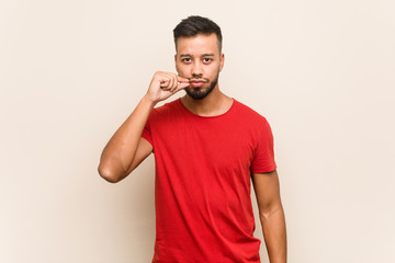 Young south-asian man with fingers on lips keeping a secret.