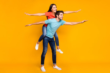 Fototapeta na wymiar Full size photo of funny guy carry lady piggyback spend summer weekend together spread arms like wings wear casual stylish blue orange t-shirts jeans isolated yellow color background