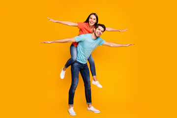 Fototapeta na wymiar Full length photo of funny guy carry lady piggyback spend summer weekend together spread arms like wings wear casual stylish blue orange t-shirts jeans isolated yellow color background