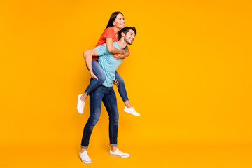 Fototapeta na wymiar Full length photo of two funny people guy carrying lady piggyback meet summer adventures together wear casual trendy blue orange t-shirts jeans isolated yellow color background
