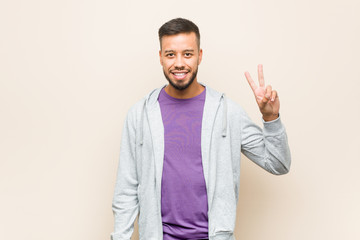 Young south-asian man joyful and carefree showing a peace symbol with fingers.