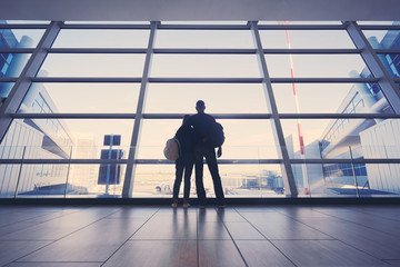 Fototapeta na wymiar Traveling concept. Back view of loving couple in casual wear standing near the window of international airport terminal.