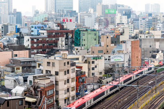 Tokyo, Japan - March 30, 2019: Shinjuku cityscape view buildings residential area on cloudy grey mist fog overcast day with many houses and red train with tracks