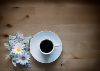 Imagen de una taza de café sobre una mesa de madera con flores