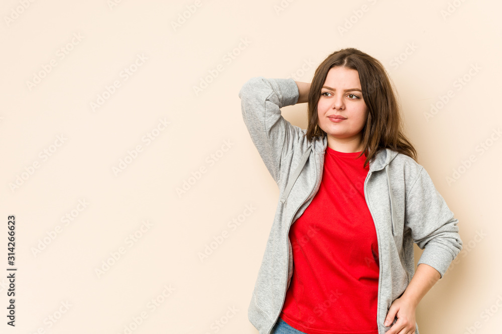 Wall mural Young sporty curvy woman touching back of head, thinking and making a choice.