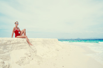 Fototapeta na wymiar Vacation on the seashore.Young woman in red swimsuit sitting on the beautiful tropical white sand beach.