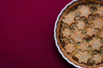 Homemade open pie with meat and potatoes on shortcrust pastry garnished with stars from the dough and sesame seeds on maroon tablecloth. Top view. Closeup