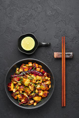 Kung Pao Paneer at black slate background. Kung Pao Paneer is a vegetarian version of chinese sichuan dish Gong Bao with paneer cheese, peanuts, chilli peppers, sauces and onion. Top view. Copy space