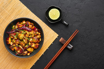 Kung Pao Paneer at black slate background. Kung Pao Paneer is a vegetarian version of chinese sichuan dish Gong Bao with paneer cheese, peanuts, chilli peppers, sauces and onion. Top view. Copy space